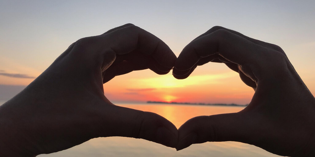 Hands making heart around sunset